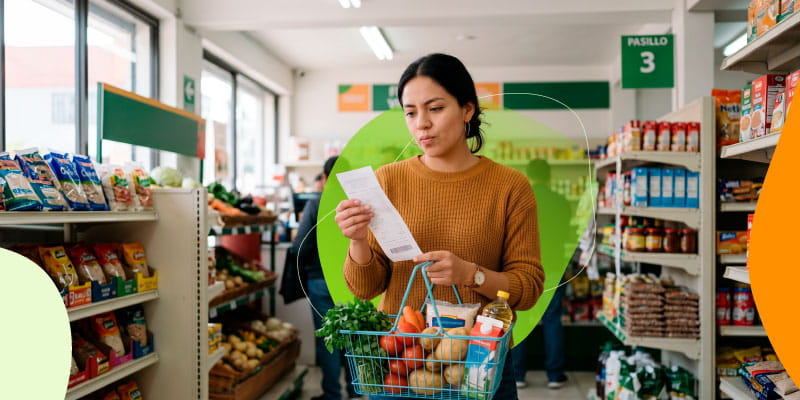 Mujer revisando el ticket de compra junto a su carrito en el supermercado.